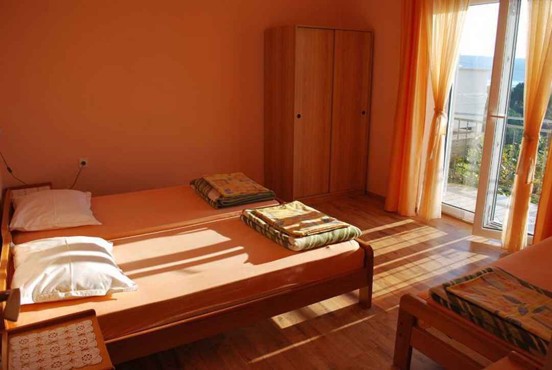 Ein Schlafzimmer mit einem hölzernen Bett, einem Kleiderschrank und Blick durch ein großes Fenster.
