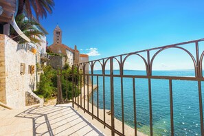 A coastal walkway with stone buildings, a church tower, and a metal railing overlooking the sea. - Holiday apartment with air conditioning and terrace (Supetarska Draga)