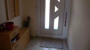 Een gang met een witte deur, een houten kast met lades, een rode pot en een kleine plant.