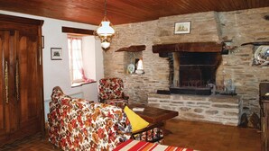 A cozy room with a stone fireplace, wooden ceiling, and a floral sofa. - 2 bedroom awesome home in Garlan (Garlan)
