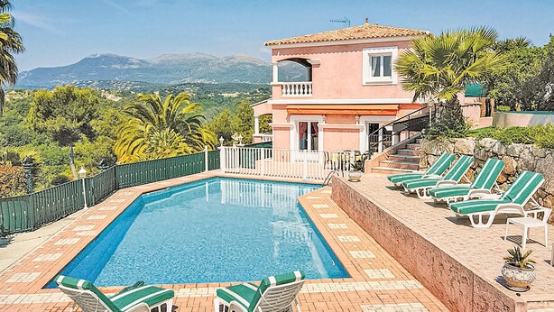 Un espace piscine offrant une vue dégagée sur les montagnes en arrière-plan, un bâtiment à deux étages doté d’un balcon et plusieurs chaises longues.