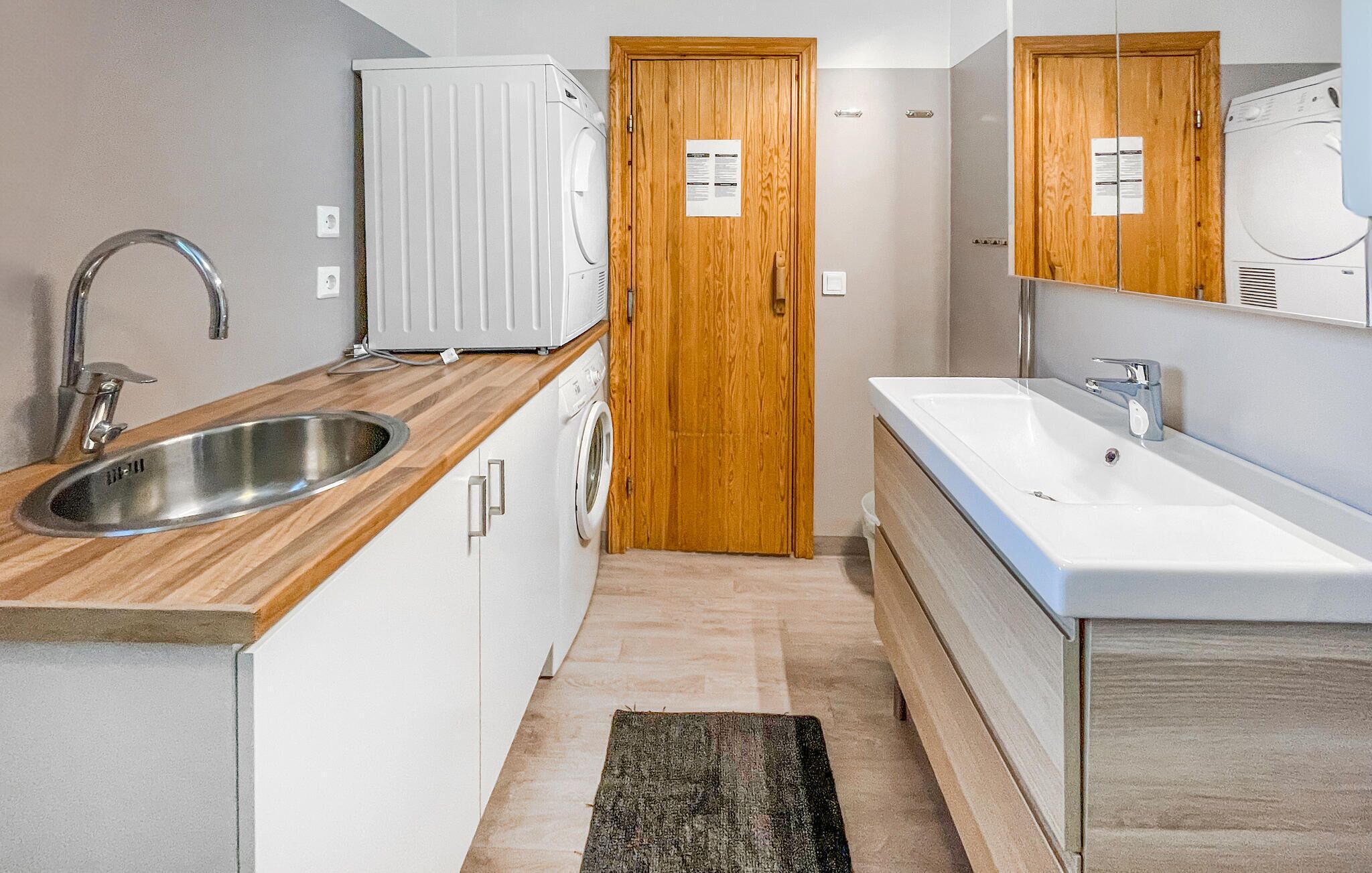 Une petite cuisine équipée d’un évier, d’une porte en bois et d’un lave-linge blanc.