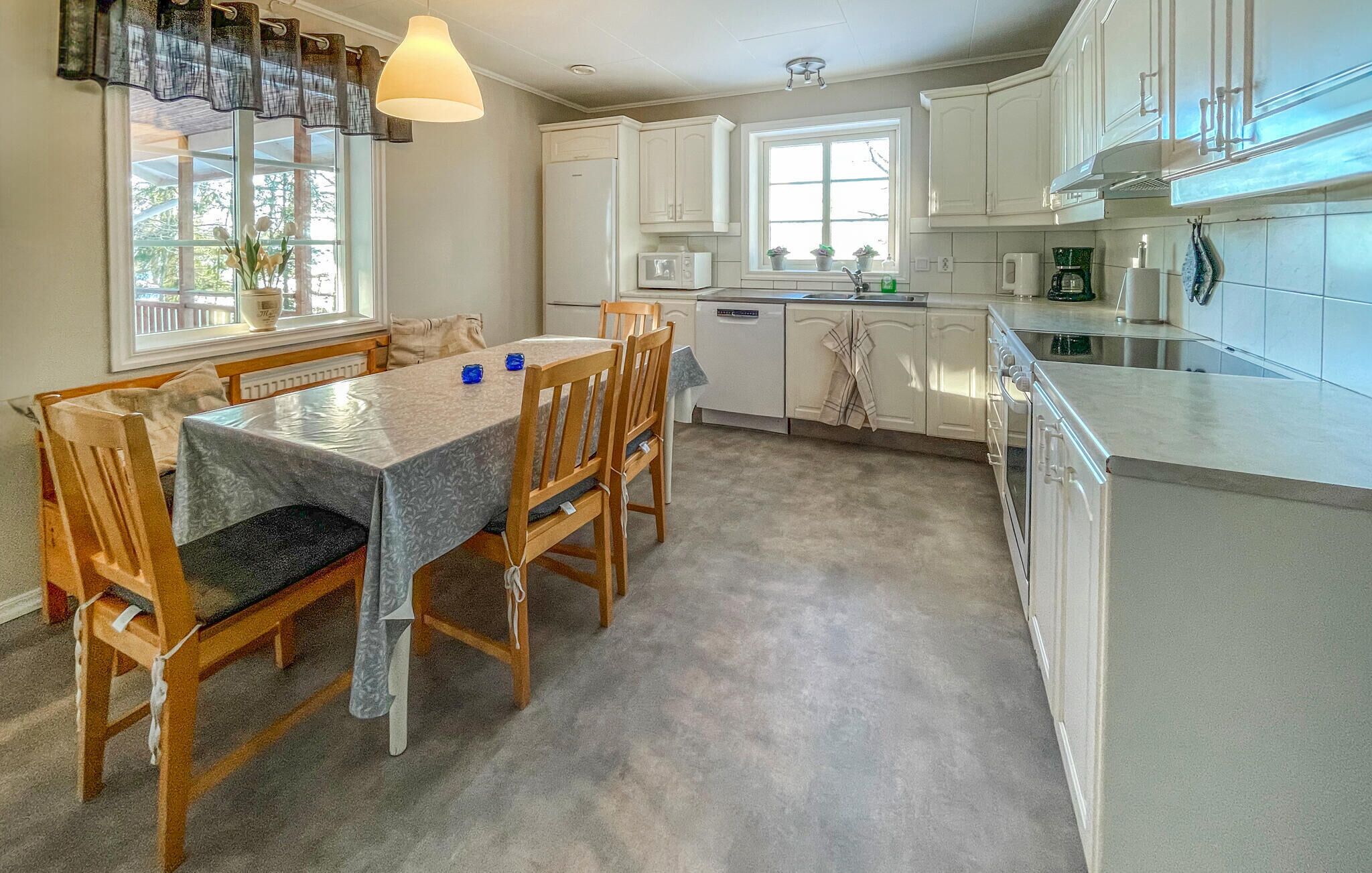 Une cuisine moderne avec des meubles blancs, une table à manger avec des chaises, une fenêtre avec des rideaux et un luminaire suspendu.