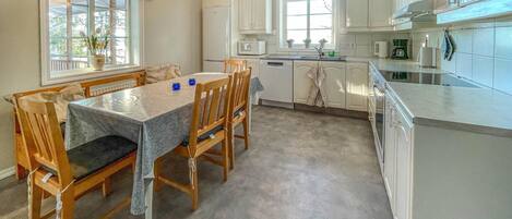 Une cuisine moderne avec des meubles blancs, une table à manger avec des chaises, une fenêtre avec des rideaux et un luminaire suspendu.