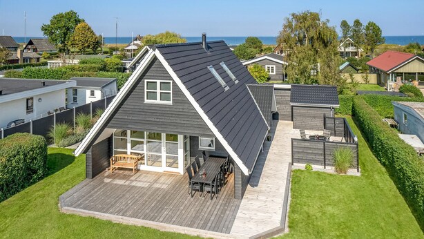 Une maison moderne avec un toit en pente, une terrasse dotée de mobilier d’extérieur et une vue sur la mer.