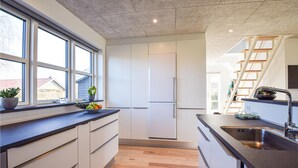 Une cuisine moderne avec un plancher en bois, des armoires blanches, un comptoir noir et une fenêtre donnant sur une maison.