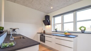 Une cuisine moderne dotée d’un plan de travail foncé, de meubles blancs, d’un four encastré et d’une fenêtre donnant sur l’extérieur.