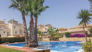 A swimming pool surrounded by palm trees and a building with multiple balconies.