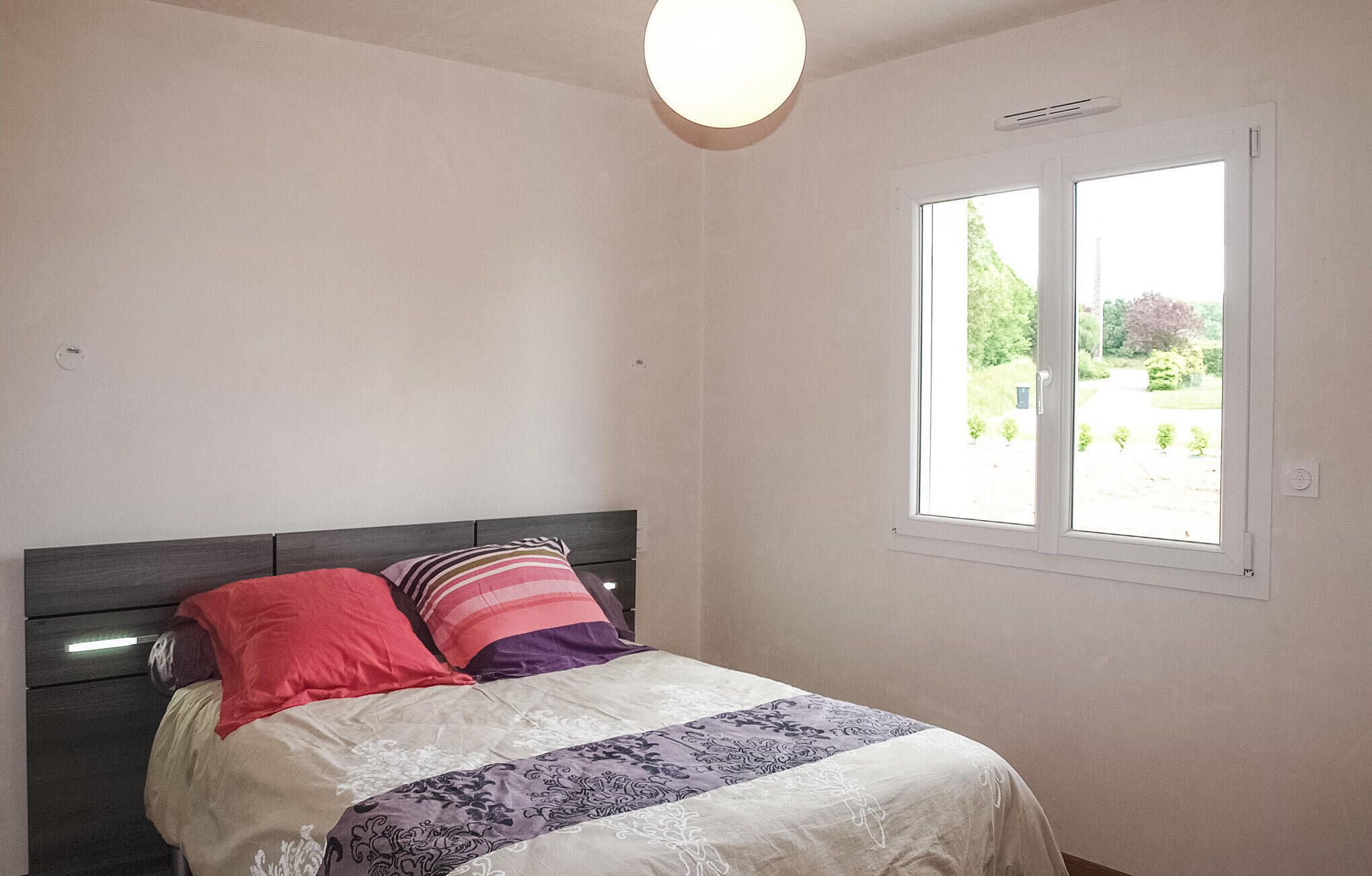 Een slaapkamer met een bed, een raam met uitzicht op groen en een plafondlamp.