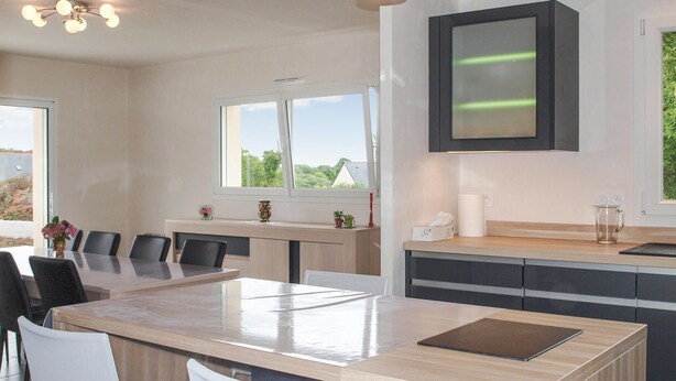A modern kitchen with a central island, a dining area with chairs, and a large window providing a view of greenery outside. - 3 bedroom beautiful home in Louargat (Louargat)