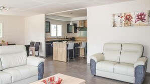 A modern living room with two white leather sofas, a wooden coffee table, and a kitchen area with a bar counter and chairs. - 3 bedroom beautiful home in Louargat (Louargat)