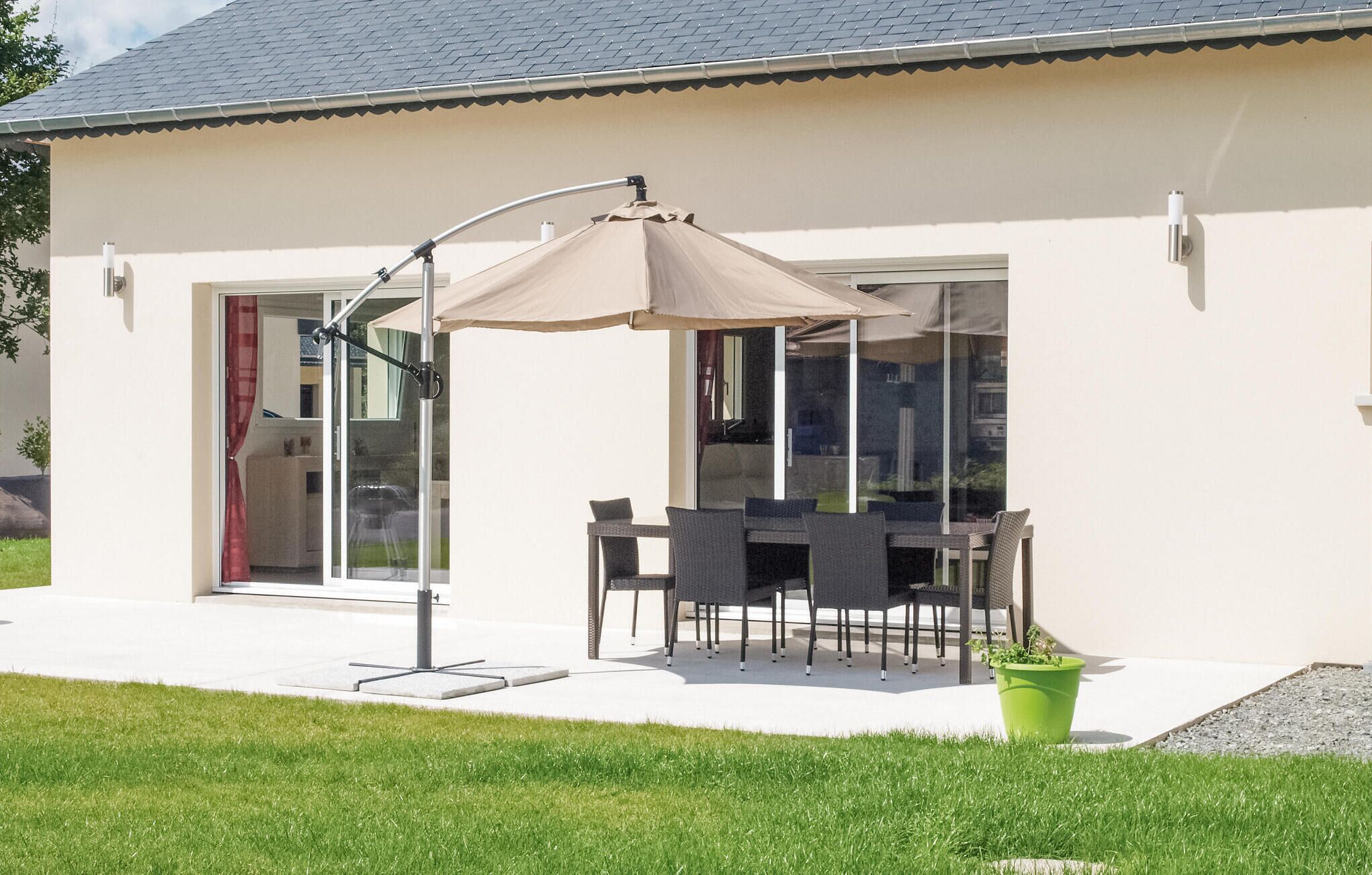 Une maison moderne dotée d’un patio comprenant une table et des chaises, un grand parasol et une plante verte en pot.