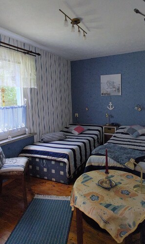 Ein Zimmer mit zwei Betten, einem Sessel, einem kleinen Tisch mit Kerze und einem Fenster mit Vorhängen.