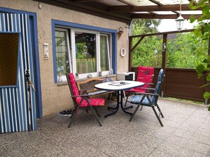 Un patio con mesa y sillas, una zona de estar techada y vista a zonas verdes.