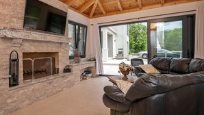 A modern living room with a stone fireplace, leather sofa, and a large TV.