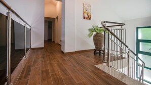 A modern interior with a wooden floor, a staircase with metal railings, a potted plant, and a painting on the wall.
