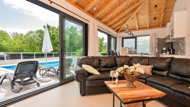 A modern living room with a leather sofa, a wooden coffee table, and a glass door leading to a pool.
