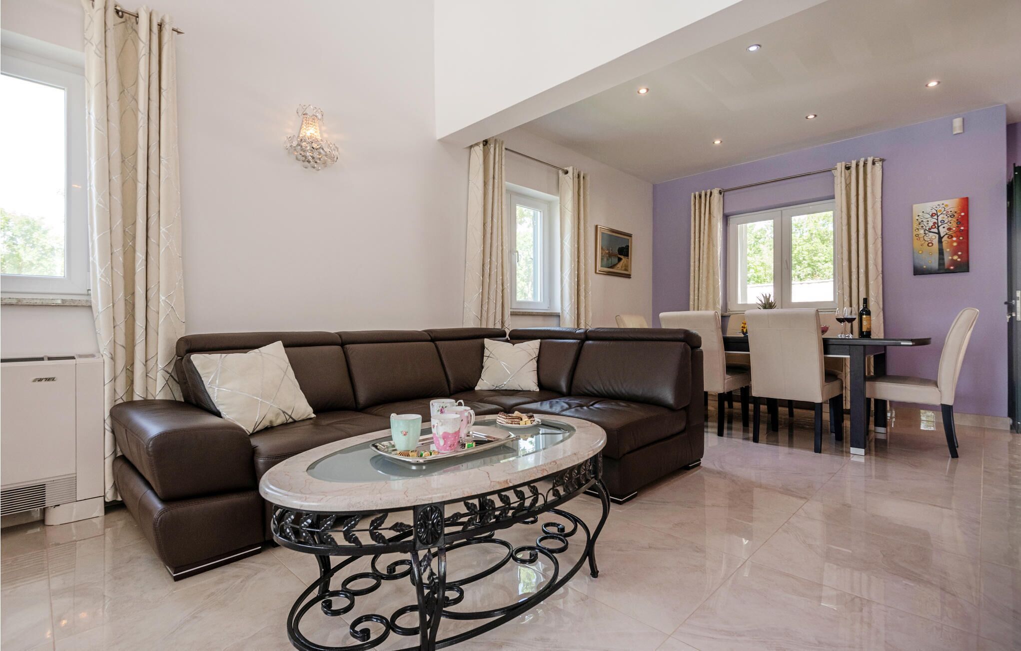 A modern living room with a brown leather sofa, a glass-top coffee table, and a dining area with a table and chairs.