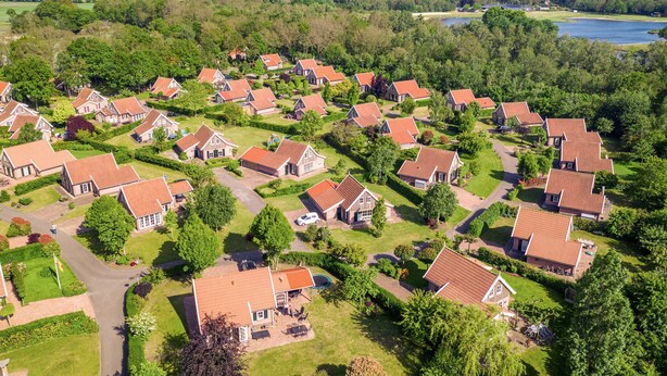 A residential area with houses having red-tiled roofs, surrounded by greenery and a lake. - Buitengoed Het Lageveld - 65 (Hoge Hexel)