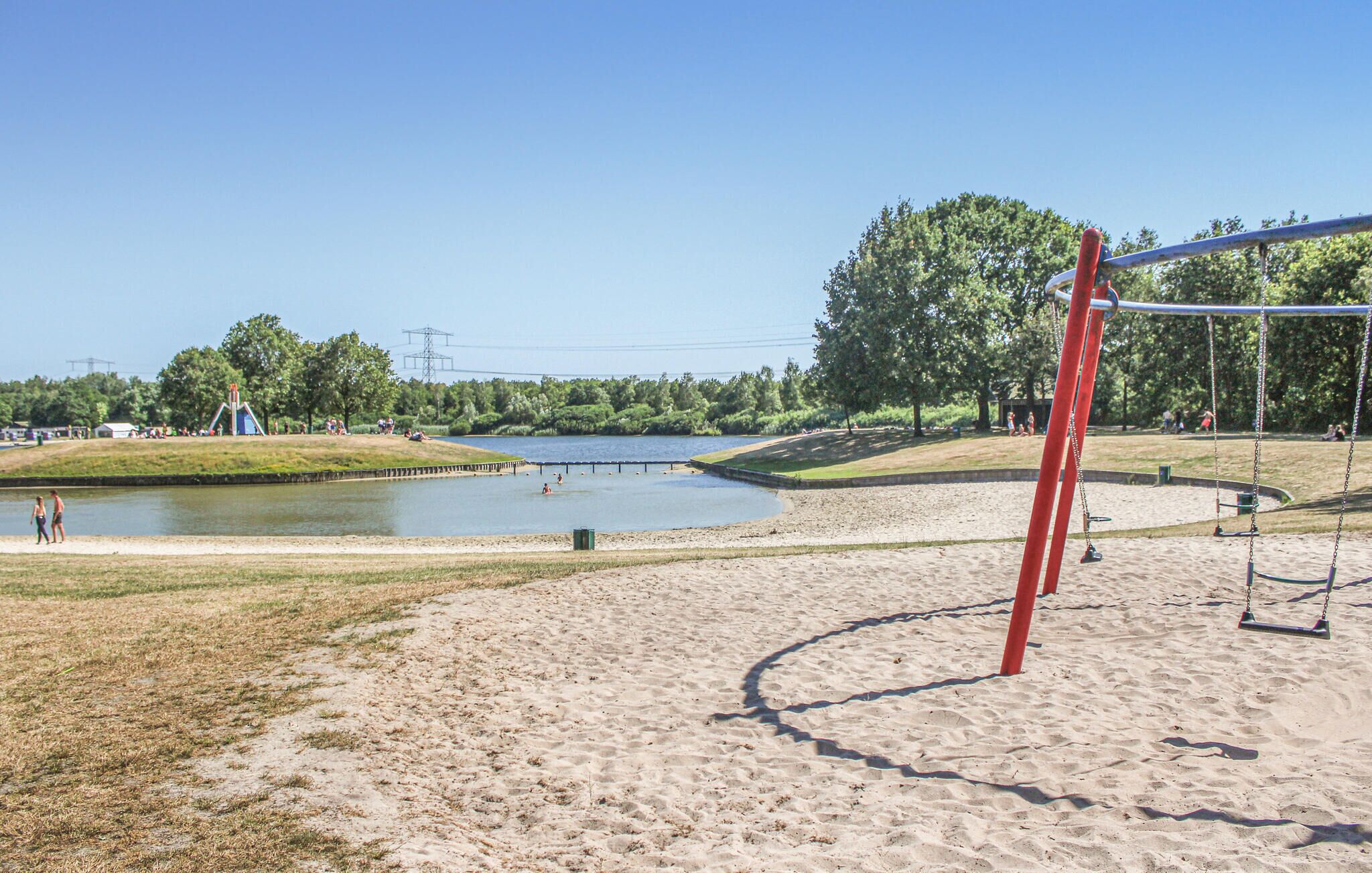 Een zandstrand met een schommel en een waterlichaam op de achtergrond.