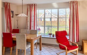 A dining room with a wooden table and chairs, a radiator, and a window with curtains.