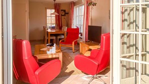 A room with a glass door, a dining table with chairs, a TV, and red chairs. - Buitengoed Het Lageveld - 65 (Hoge Hexel)