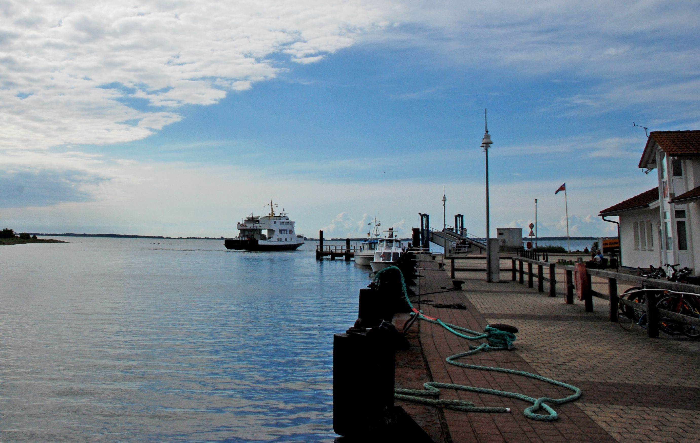 A waterfront dock with boats, a lighthouse, and a pedestrian walkway.