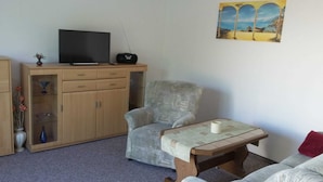 A living room with a grey armchair, a wooden cabinet, a television, and a painting on the wall.