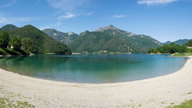 A serene lakeside view with mountains in the background and a sandy beach in the foreground. - Holiday apartment with balcony and mountain view (Locca)