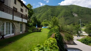 A building with a stone facade, a balcony, and a grassy courtyard with a picnic table. - Holiday apartment with balcony and mountain view (Locca)