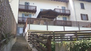 A building with multiple balconies, a staircase leading to the entrance, and a wooden fence. - Holiday apartment with balcony and mountain view (Locca)