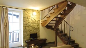 A living room with a stone wall, a wooden staircase, a television, and a sofa. - Holiday apartment with balcony and mountain view (Locca)