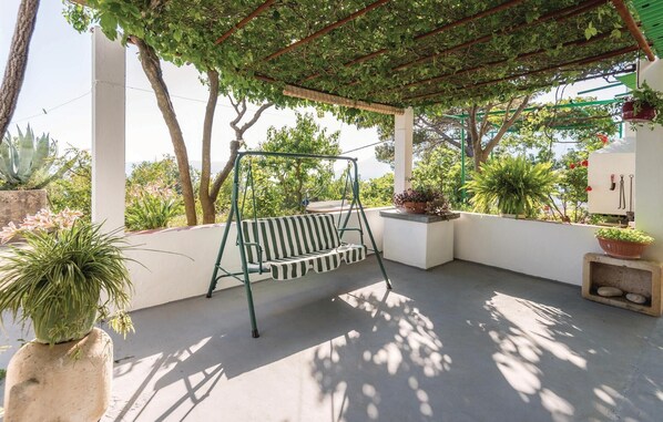 A covered patio with a swing, potted plants, and a view of the surrounding landscape.