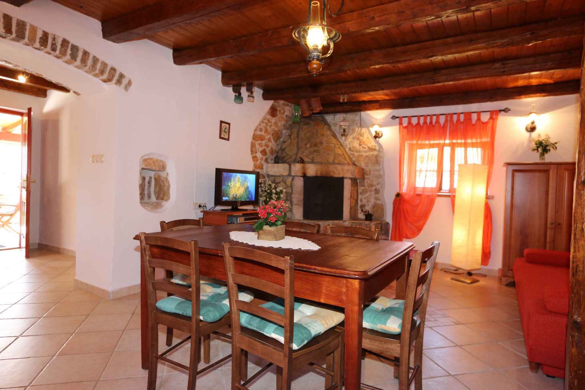 A dining area with a stone fireplace, wooden ceiling, and a television on a table.