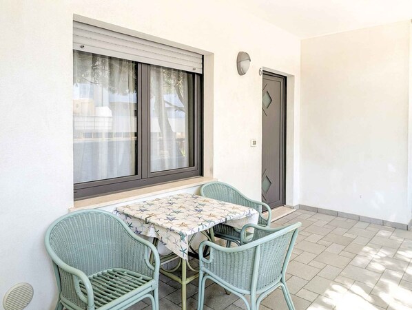 A small outdoor dining area with a table and four chairs, a window with blinds, and a door.