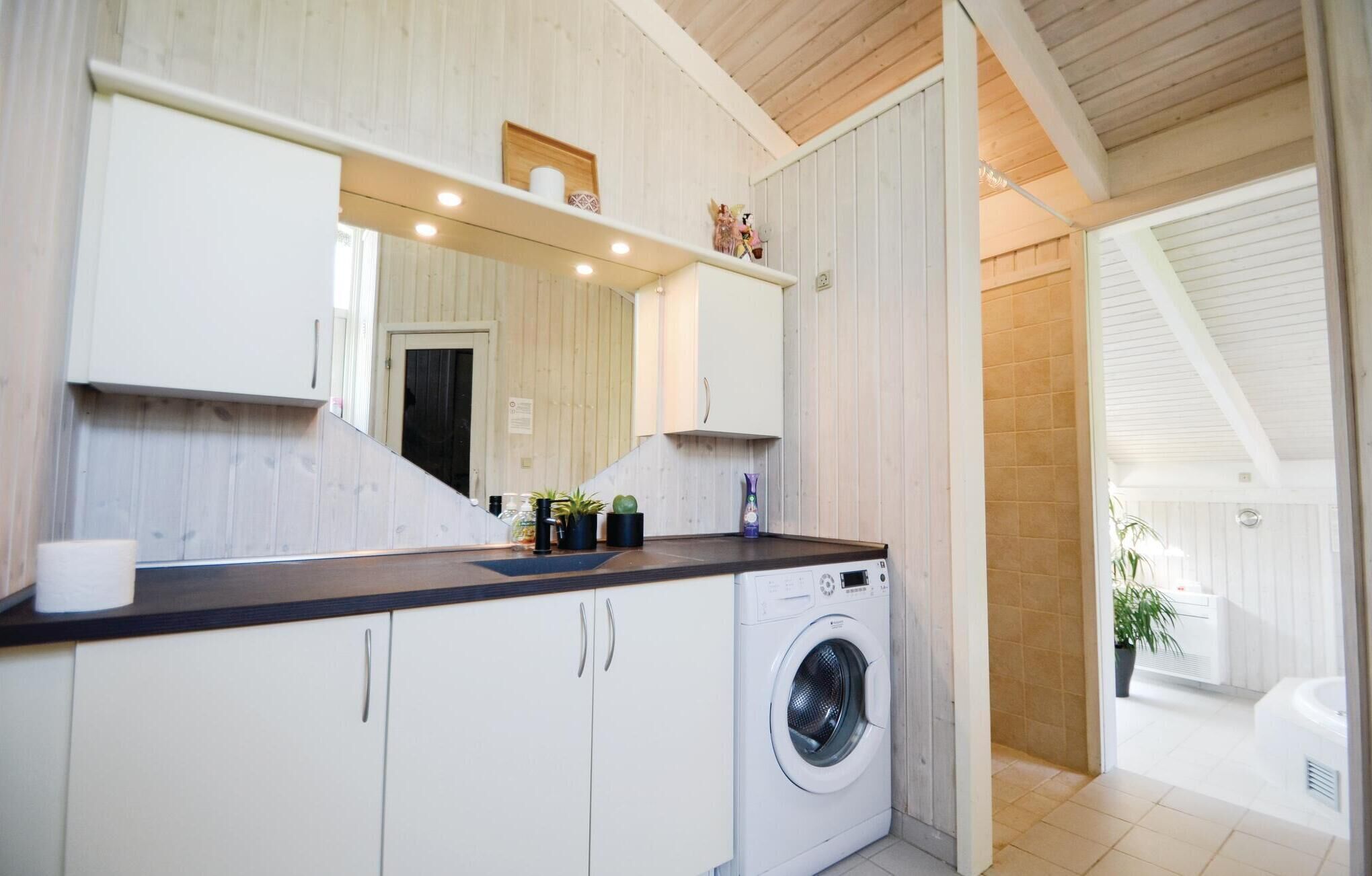 A compact kitchen with a built-in washing machine, wooden cabinets, and a large mirror above the counter.