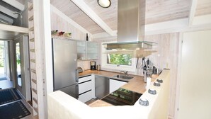 Une cuisine moderne dotée d’un réfrigérateur en acier inoxydable, d’une plaque de cuisson en verre et d’une fenêtre laissant entrer la lumière naturelle.