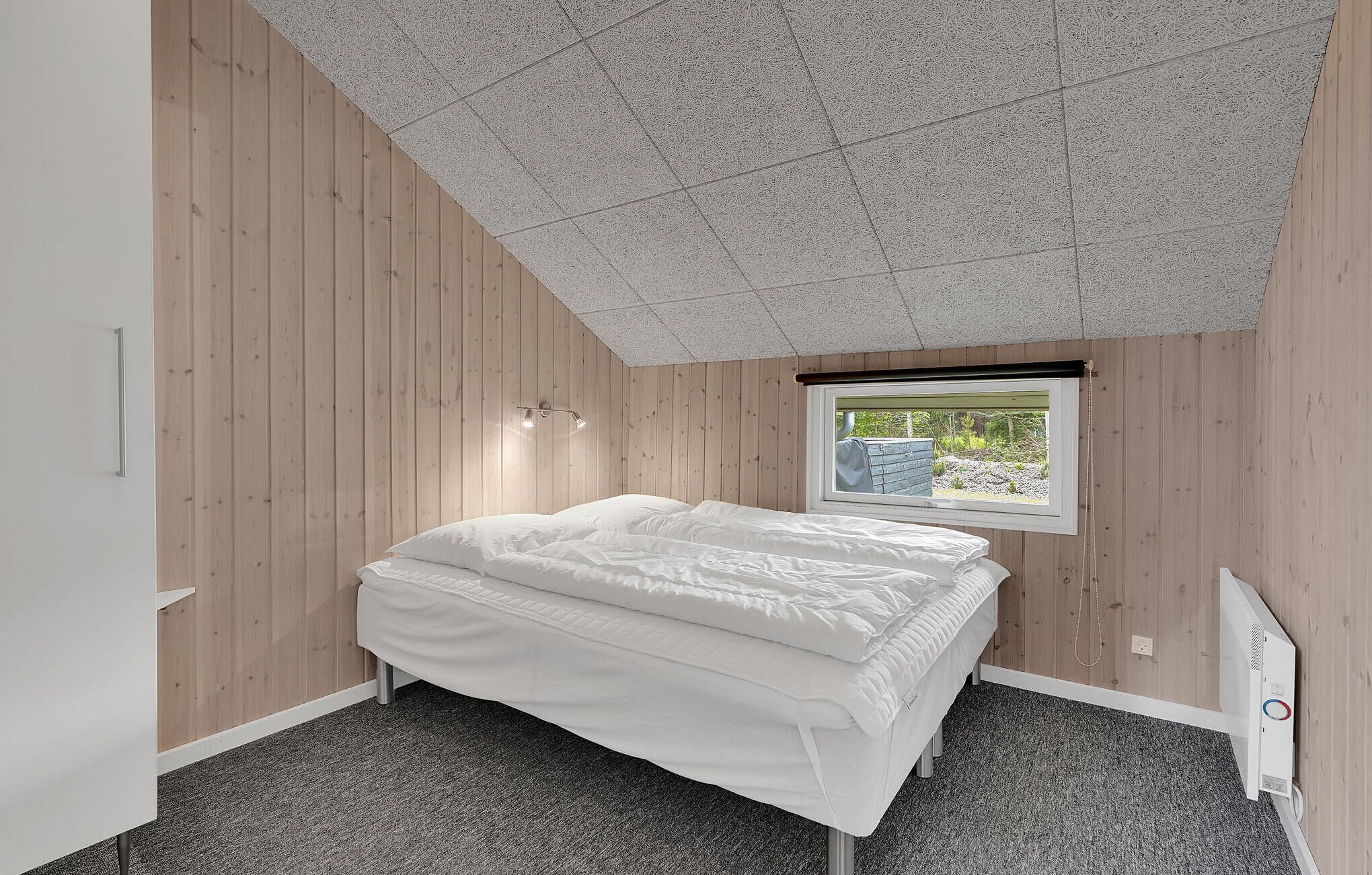 Una camera da letto con un letto, una finestra vista su del verde, un termosifone e pareti in legno.