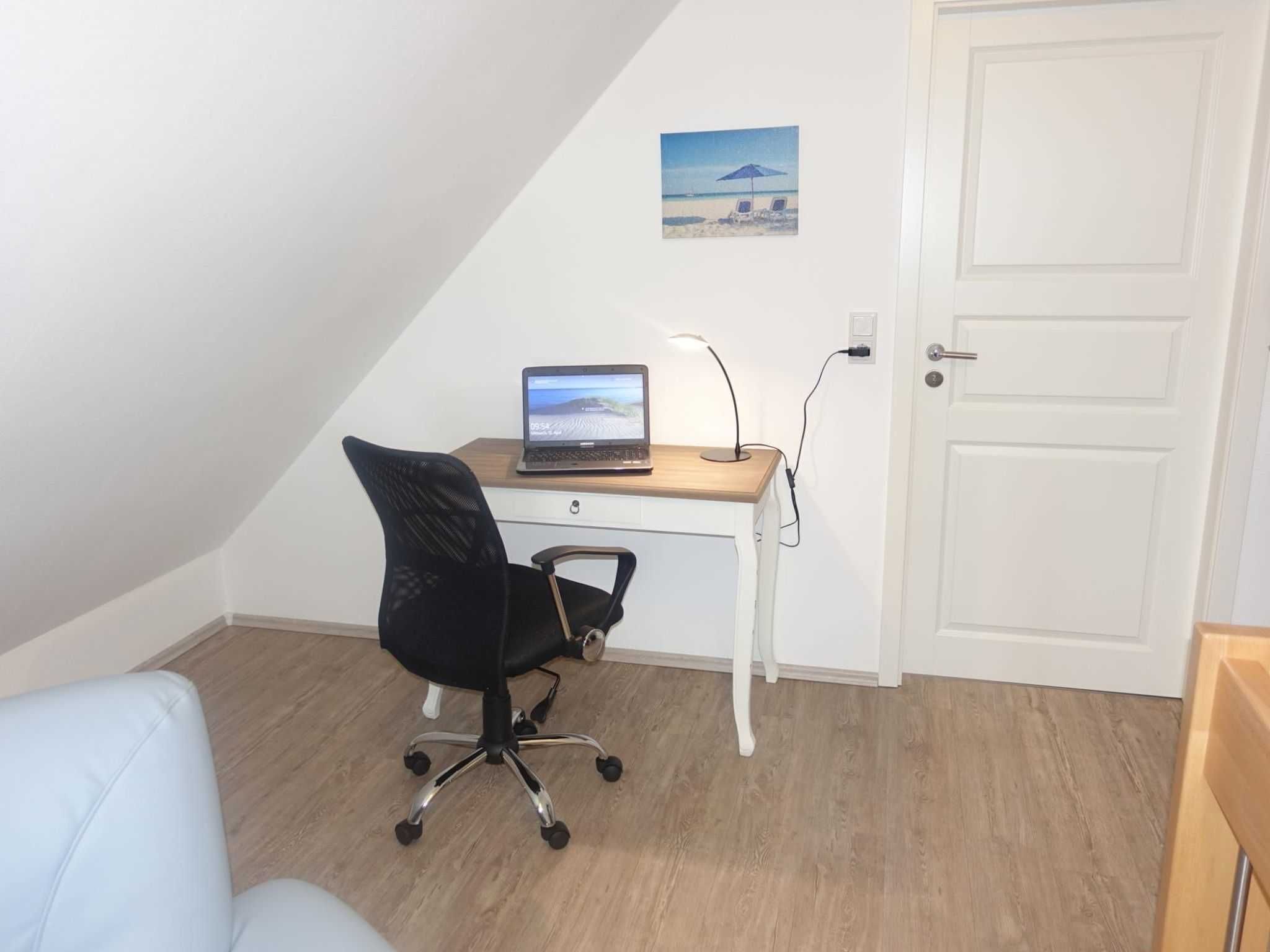 Une petite pièce avec un bureau, un ordinateur portable, une chaise et une porte.