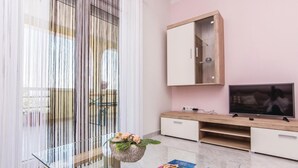 Un salon moderne avec une table basse en verre, un téléviseur à écran plat, des meubles en bois et un grand miroir.