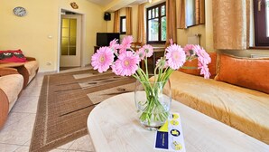 Un salón con un sofá, una mesa de centro con un jarrón de flores, un reloj y un televisor al fondo.