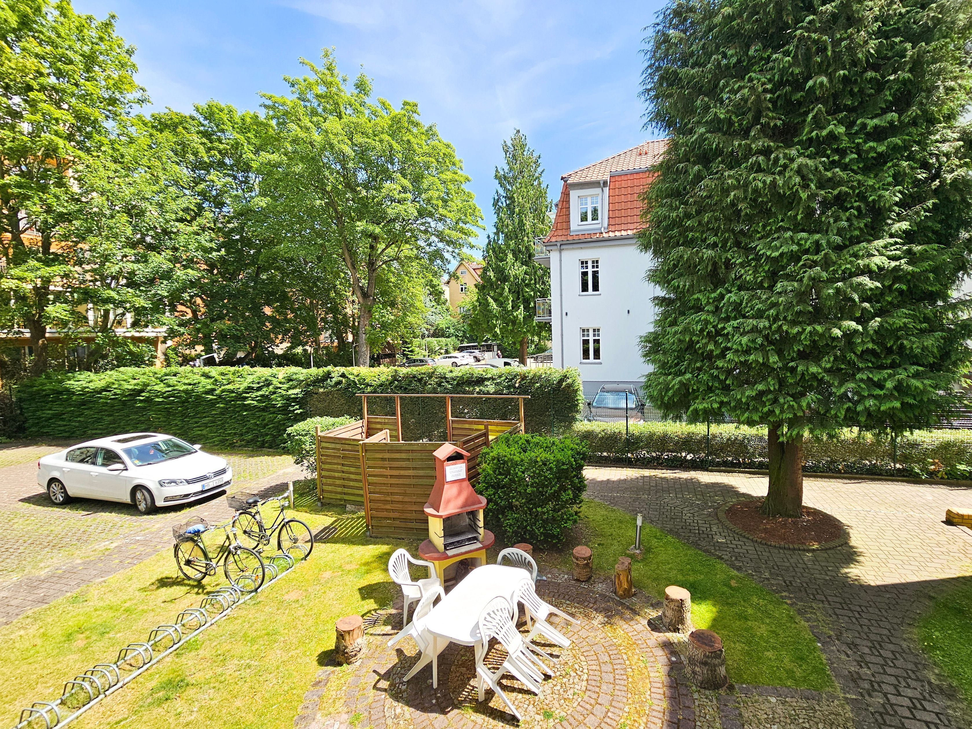 Une cour avec un espace barbecue, une voiture blanche et un vélo.
