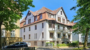 Un edificio de varios pisos con un estilo arquitectónico tradicional, que presenta una combinación de fachadas blancas y marrones, múltiples ventanas y un balcón en el piso superior.