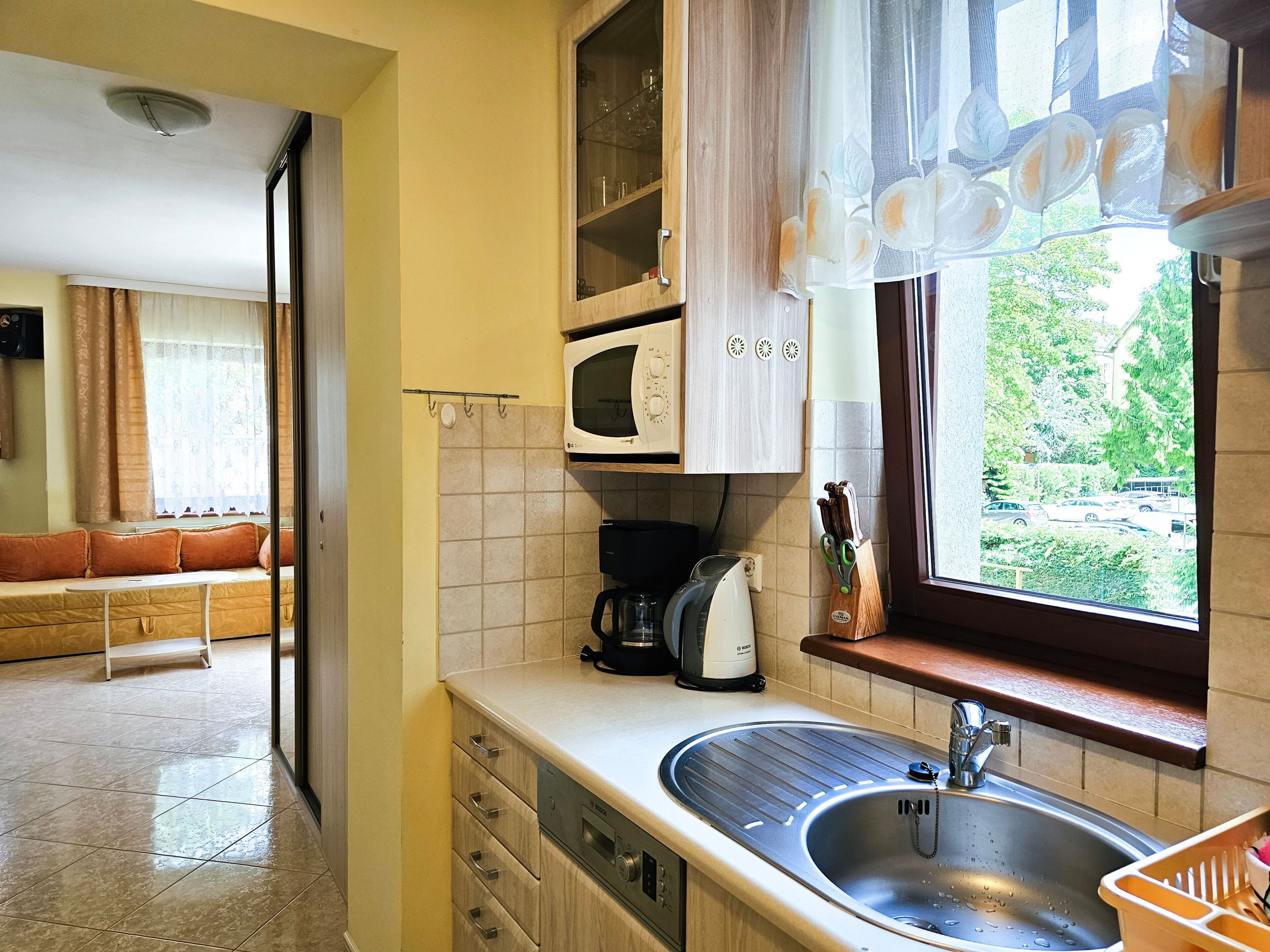 A kitchen with a sink, microwave, and coffee maker. There is a window with a view of greenery outside.