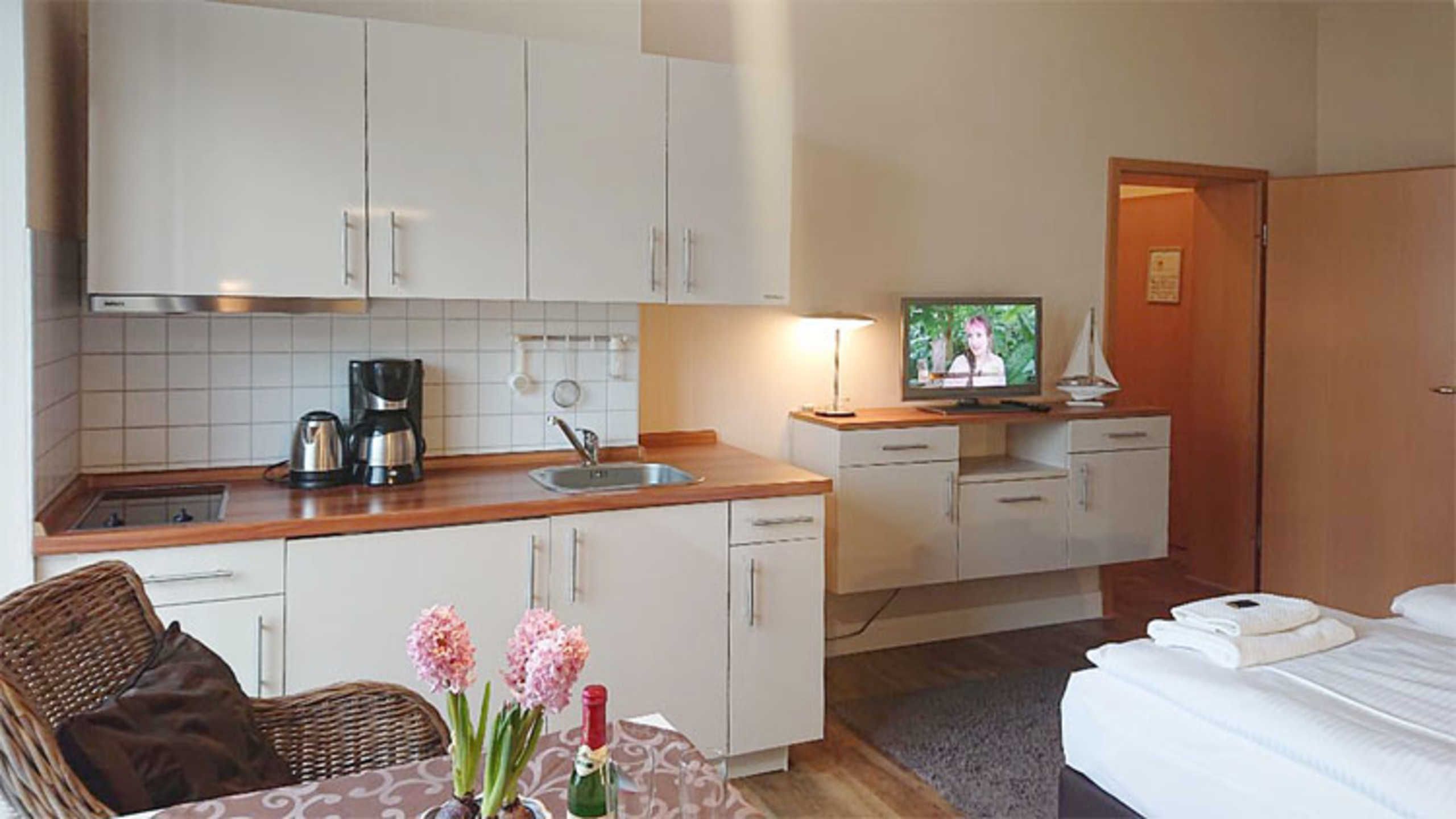 A compact hotel room with a kitchenette, a dining area, a television, and a bed.