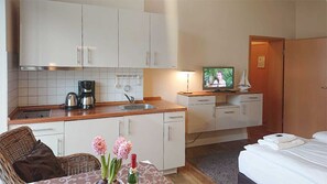 Una habitación de hotel compacta con kitchenette, comedor, televisor y cama.