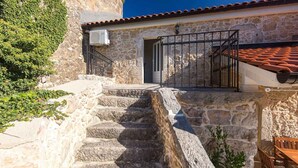 A stone building with a staircase leading to a door, a metal gate, and a tiled roof. - Holiday home with terrace and barbecue (Polje/Krk)