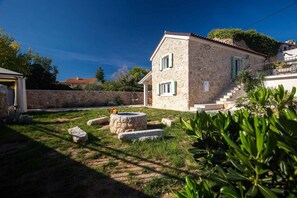 Traditional stone house with a pitched roof and small porch, surrounded by a well-maintained garden and a stone well.