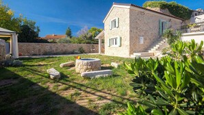 A stone house with a stone wall, a small garden with rocks and plants, and a staircase leading to the entrance. - Holiday home with terrace and barbecue (Polje/Krk)