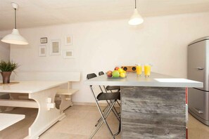 A kitchen with a white table, black chairs, a wooden island, and a stainless steel refrigerator.